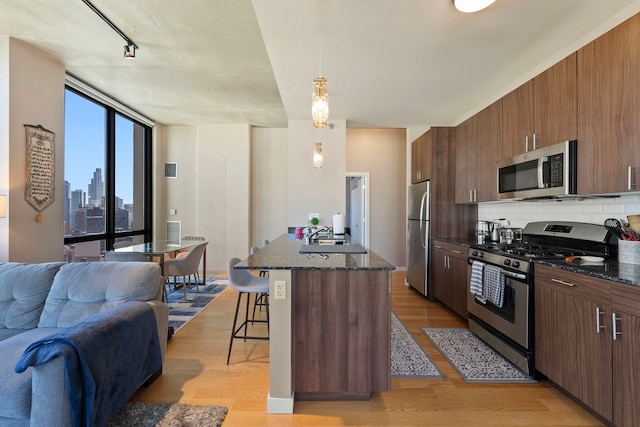 kitchen featuring a breakfast bar area, tasteful backsplash, hanging light fixtures, light wood-type flooring, and stainless steel appliances