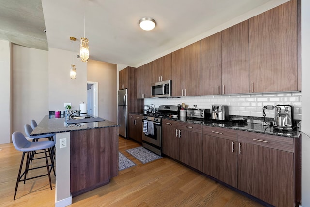 kitchen featuring appliances with stainless steel finishes, decorative light fixtures, light hardwood / wood-style floors, and dark stone counters