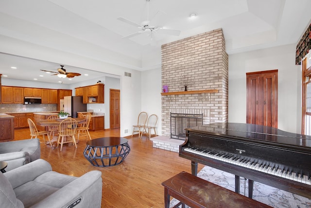 living room with visible vents, a brick fireplace, light wood-type flooring, and a ceiling fan