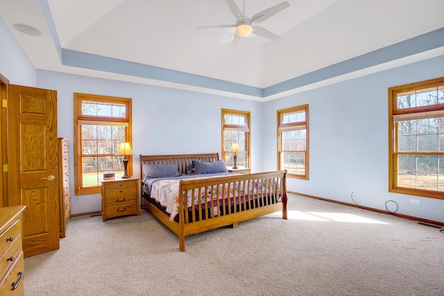 bedroom with light carpet, multiple windows, baseboards, and a tray ceiling