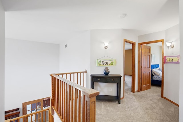 hall featuring baseboards, an upstairs landing, visible vents, and light carpet