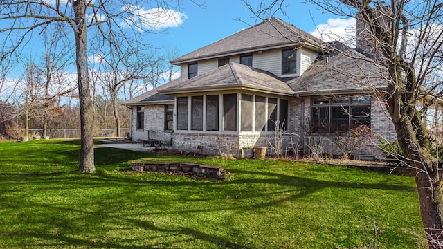 rear view of house with a yard, roof with shingles, a chimney, and a sunroom