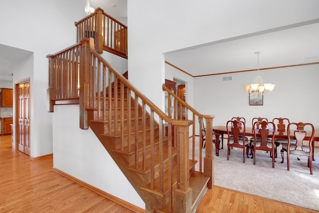 staircase featuring wood finished floors, baseboards, an inviting chandelier, a towering ceiling, and crown molding