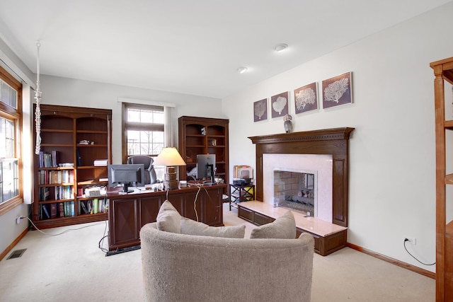 office space featuring visible vents, a fireplace with raised hearth, light colored carpet, and baseboards