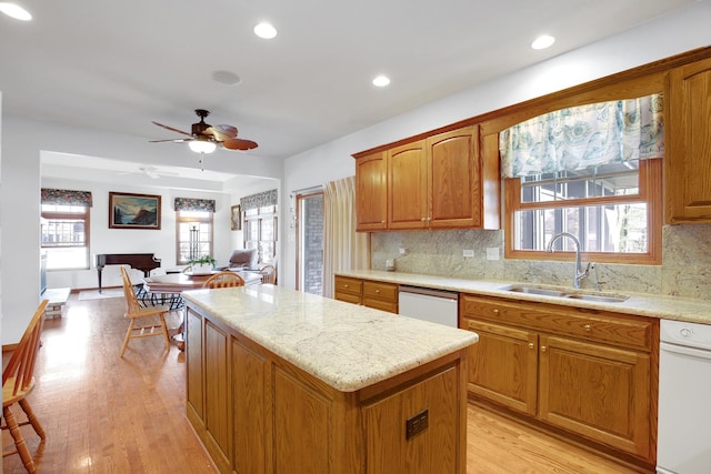 kitchen with a kitchen island, light wood-style flooring, brown cabinets, white dishwasher, and a sink