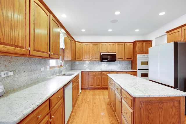 kitchen with a kitchen island, black electric stovetop, light stone countertops, double oven, and a sink