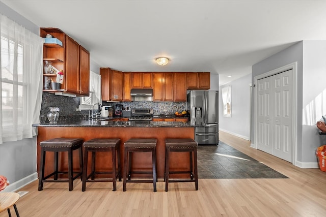 kitchen featuring sink, light hardwood / wood-style flooring, a breakfast bar area, appliances with stainless steel finishes, and decorative backsplash