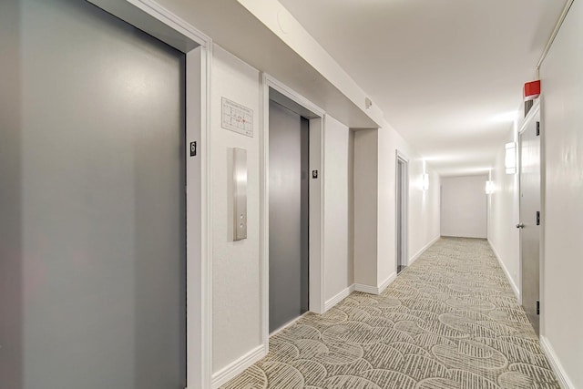 corridor featuring light carpet, baseboards, and elevator