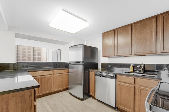 kitchen with stainless steel appliances, light wood finished floors, a sink, and brown cabinets