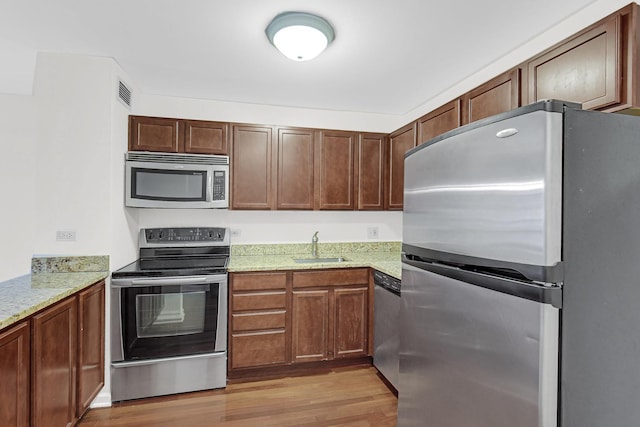 kitchen with visible vents, light stone countertops, stainless steel appliances, light wood-type flooring, and a sink