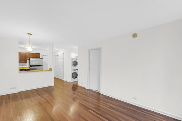 unfurnished living room with dark wood-style floors, stacked washer and dryer, and baseboards