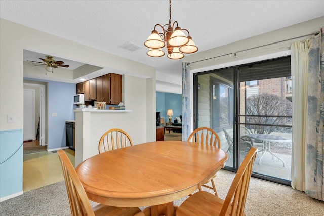 carpeted dining space with ceiling fan with notable chandelier and a textured ceiling