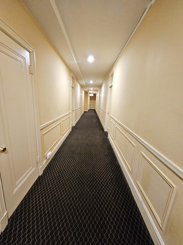 corridor with dark colored carpet, a decorative wall, and recessed lighting