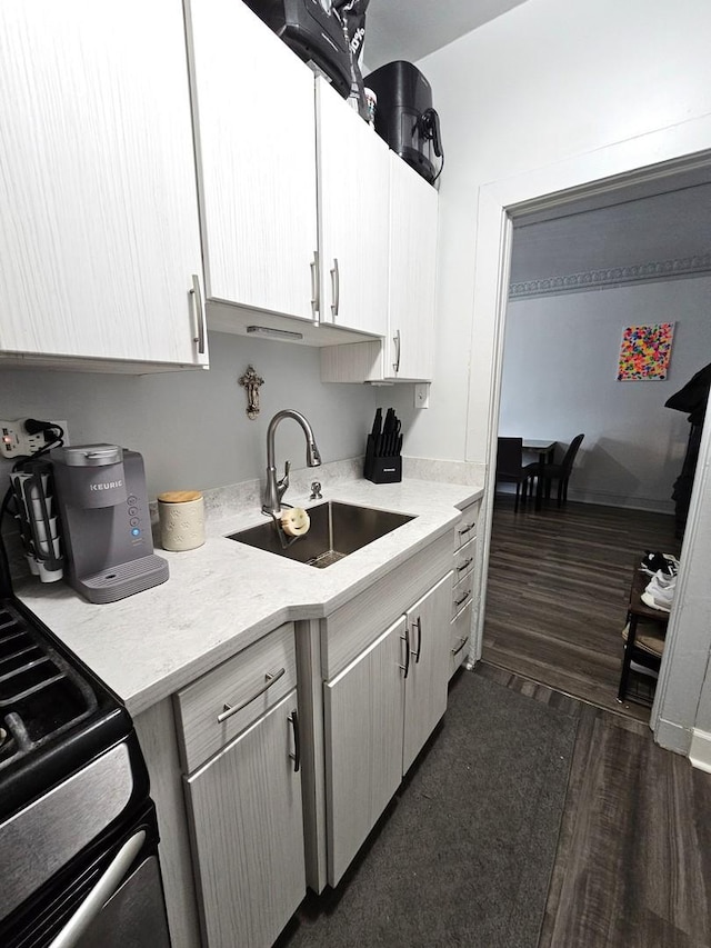 kitchen featuring dark wood-style floors, light countertops, a sink, and gas range oven