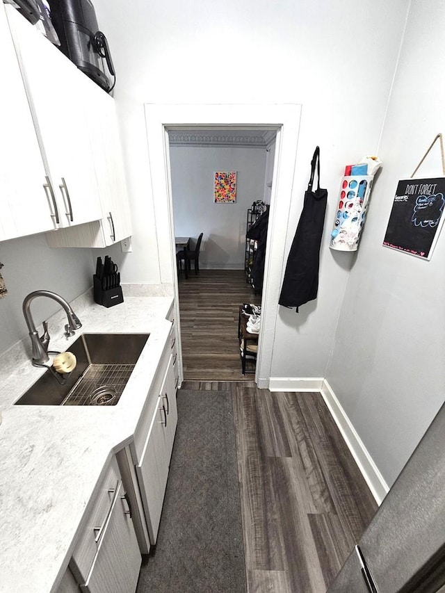 kitchen featuring light stone counters, a sink, white cabinetry, baseboards, and dark wood finished floors