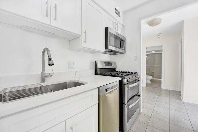 kitchen with sink, white cabinetry, light tile patterned floors, appliances with stainless steel finishes, and light stone countertops