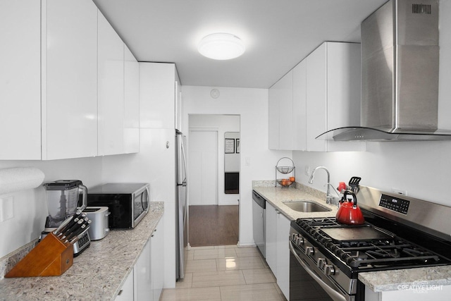 kitchen with sink, white cabinetry, light stone counters, stainless steel appliances, and wall chimney range hood