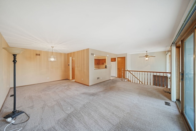 spare room with ceiling fan with notable chandelier and light colored carpet