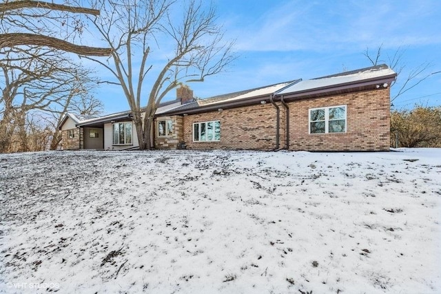 snow covered house featuring brick siding, an attached garage, and a chimney