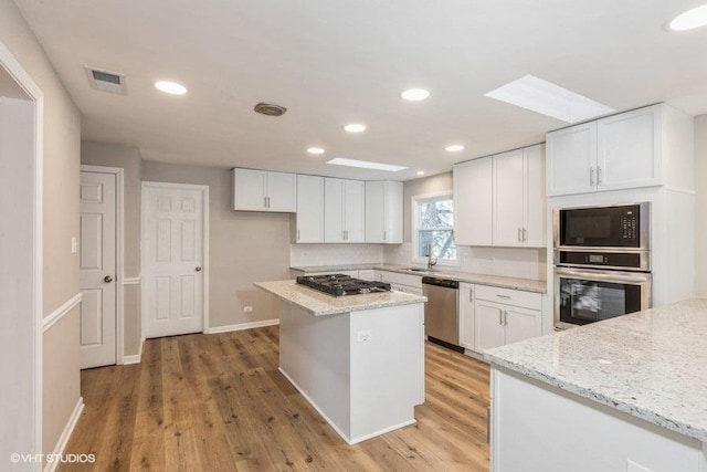 kitchen featuring light wood-type flooring, visible vents, light stone counters, white cabinetry, and appliances with stainless steel finishes