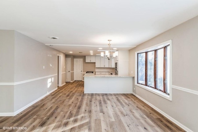 kitchen featuring light stone countertops, white cabinets, decorative light fixtures, kitchen peninsula, and light wood-type flooring