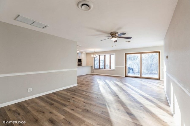 unfurnished living room with ceiling fan with notable chandelier, wood finished floors, and baseboards