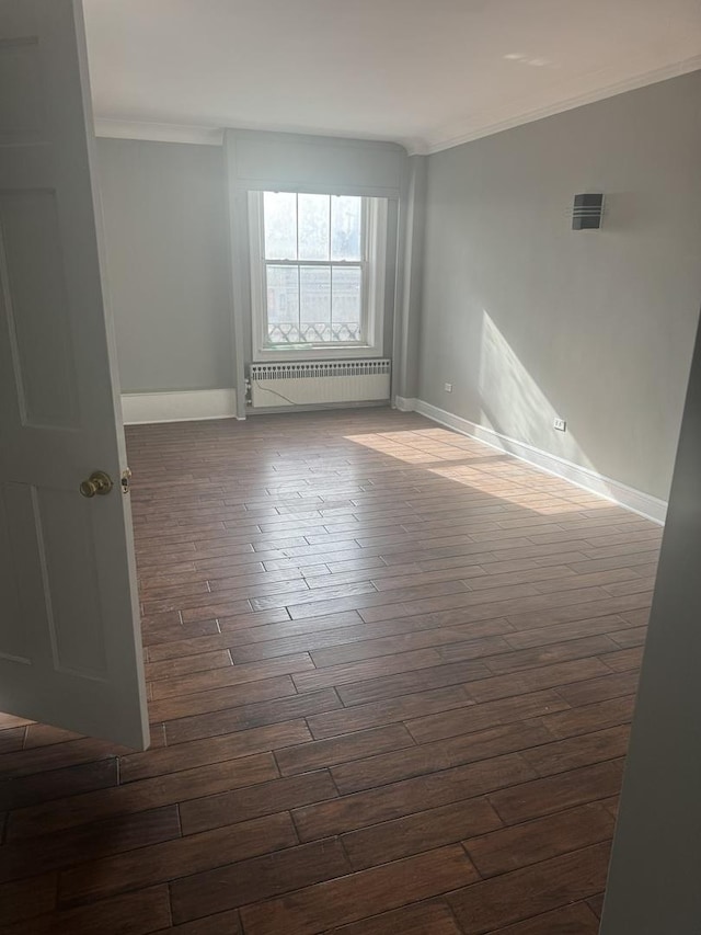 spare room with visible vents, baseboards, radiator heating unit, dark wood-type flooring, and crown molding