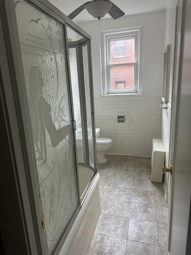 full bath with wainscoting, toilet, ceiling fan, tile patterned floors, and tile walls