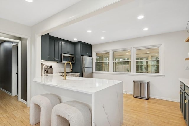 kitchen with a breakfast bar area, light hardwood / wood-style flooring, kitchen peninsula, stainless steel appliances, and light stone countertops