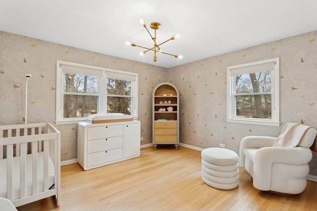 bedroom with an inviting chandelier, light hardwood / wood-style floors, and a nursery area