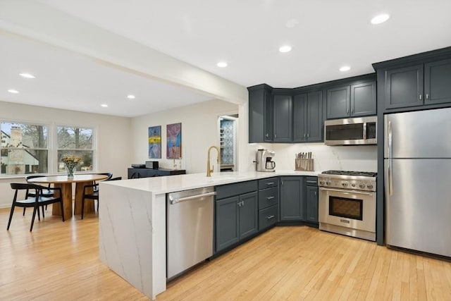 kitchen featuring sink, gray cabinetry, light hardwood / wood-style flooring, appliances with stainless steel finishes, and kitchen peninsula