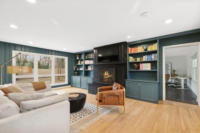 living room featuring a brick fireplace, built in features, and light wood-type flooring