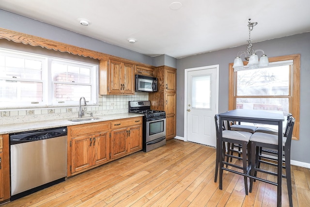 kitchen with sink, hanging light fixtures, stainless steel appliances, tasteful backsplash, and light hardwood / wood-style floors