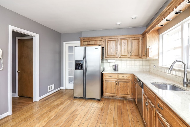 kitchen featuring sink, backsplash, stainless steel appliances, light stone counters, and light hardwood / wood-style floors