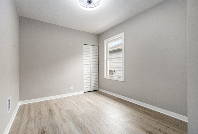 unfurnished room with a textured ceiling and light wood-type flooring