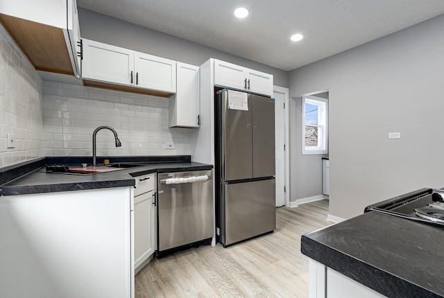 kitchen with appliances with stainless steel finishes, sink, backsplash, white cabinets, and light hardwood / wood-style floors