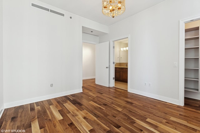 unfurnished bedroom featuring visible vents, a spacious closet, baseboards, and wood finished floors