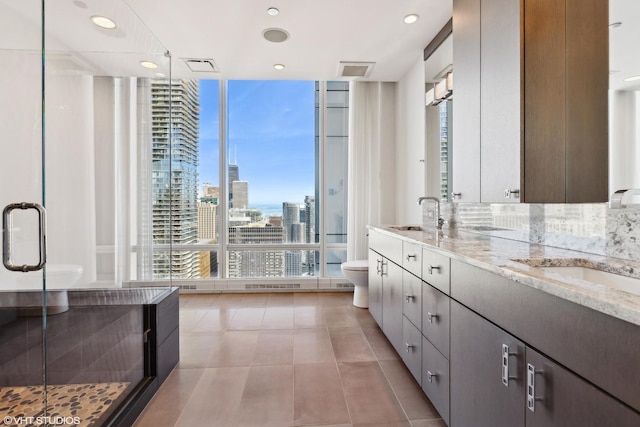 bathroom featuring toilet, a sink, a view of city, double vanity, and a wall of windows