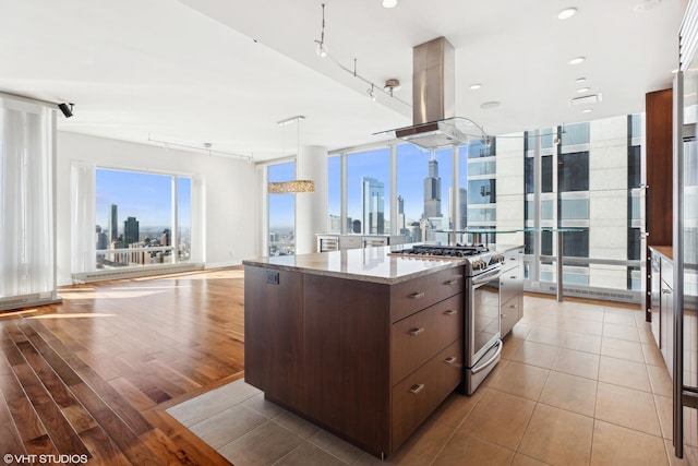 kitchen featuring stainless steel gas stove, dark brown cabinetry, open floor plan, island exhaust hood, and a city view