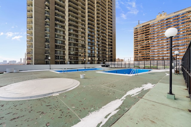 view of swimming pool with a tennis court and fence