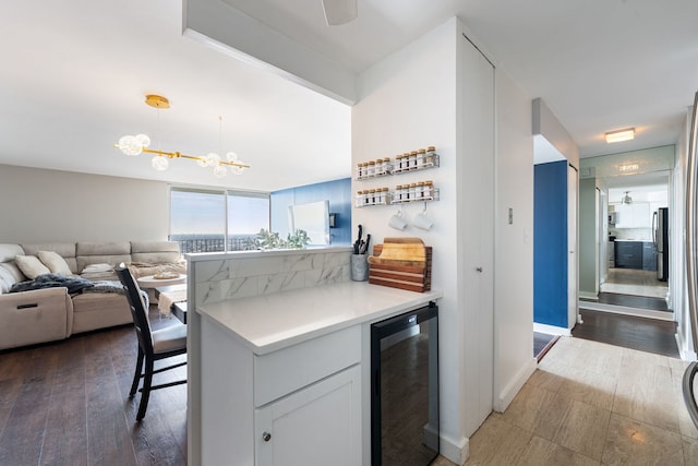 kitchen featuring wine cooler, white cabinets, open floor plan, light countertops, and hanging light fixtures