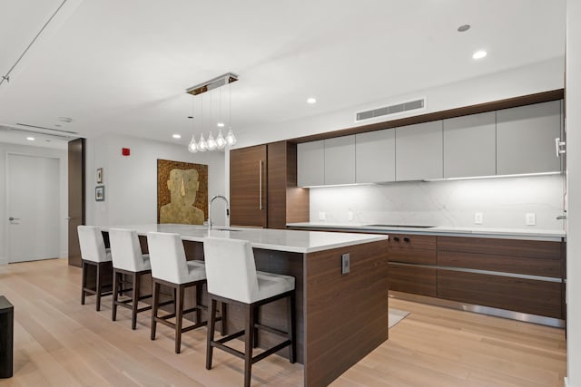 kitchen featuring sink, light hardwood / wood-style flooring, white cabinetry, an island with sink, and decorative light fixtures