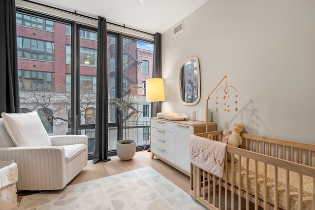 bedroom featuring floor to ceiling windows, a nursery area, and light hardwood / wood-style flooring