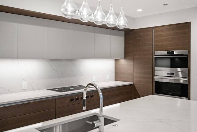 kitchen with hanging light fixtures, decorative backsplash, light stone countertops, and stainless steel double oven