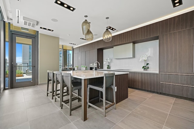 kitchen with light tile patterned floors, a breakfast bar area, hanging light fixtures, dark brown cabinetry, and a center island with sink