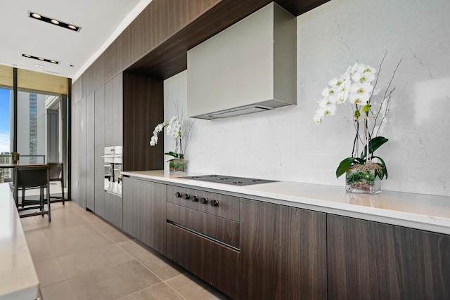 kitchen featuring light tile patterned flooring, a wall of windows, dark brown cabinets, wall chimney range hood, and black electric cooktop