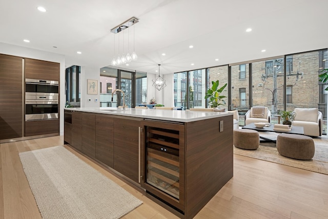 kitchen with a large island, sink, pendant lighting, wine cooler, and stainless steel double oven