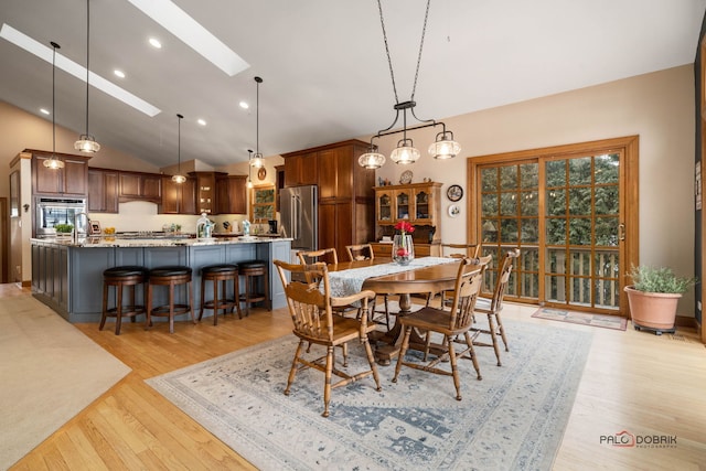 dining area featuring light hardwood / wood-style flooring, high vaulted ceiling, and a skylight