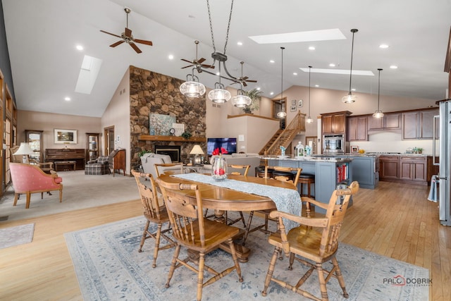 dining room featuring a stone fireplace, a skylight, high vaulted ceiling, and light wood-type flooring