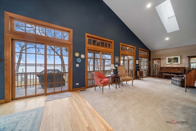 sitting room with light hardwood / wood-style floors, high vaulted ceiling, and a skylight